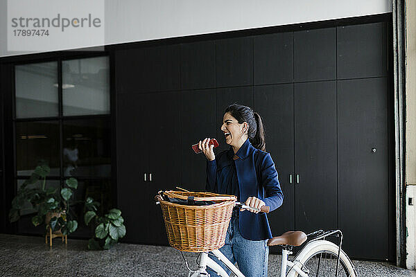 Fröhliche Geschäftsfrau  die in der Lobby über die Freisprecheinrichtung mit dem Fahrrad spricht