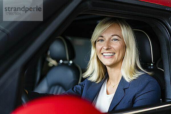 Glückliche Geschäftsfrau mit blonden Haaren sitzt im Auto