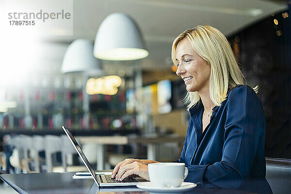 Lächelnder Freiberufler  der im Café auf dem Laptop tippt