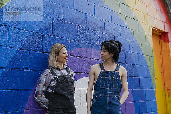 Junger Mann und Frau stehen neben einem an die Wand gemalten Regenbogen