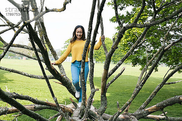 Verspielte junge Frau geht im Park auf umgestürzten Baum