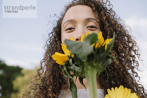 Junge Frau hält Sonnenblume vor Gesicht