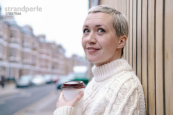 Nachdenkliche Frau mit Mehrwegbecher an der Wand