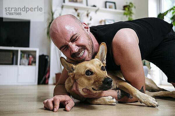 Glücklicher Mann mit geschlossenen Augen umarmt seinen Hund zu Hause