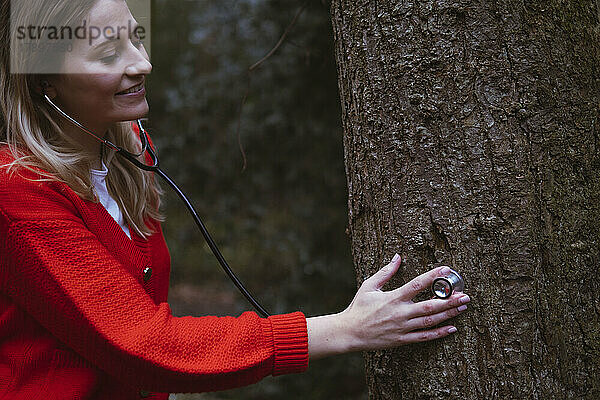 Frau mit Stethoskop untersucht Baum im Wald