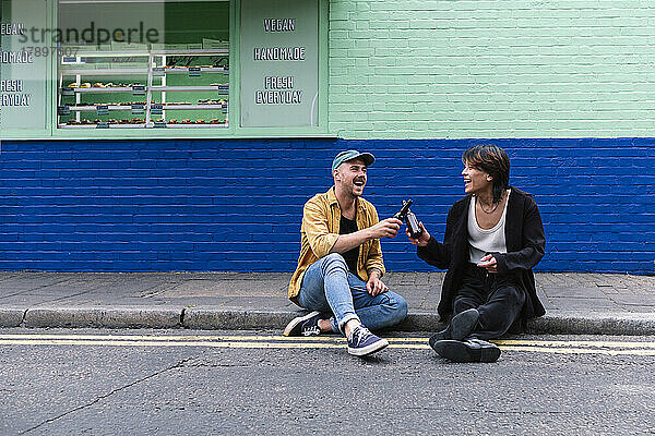 Glückliches schwules Paar  das auf dem Bürgersteig mit Flaschen prostet