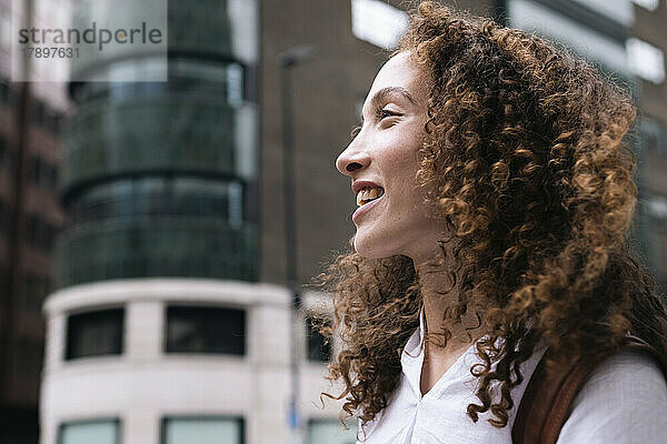 Glückliche Frau mit lockigem Haar vor dem Gebäude