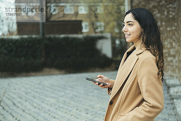 Lächelnde Frau mit Smartphone am Fußweg