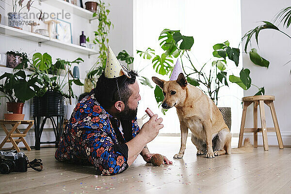 Mann mit Wurst schaut Hund mit Partyhut an