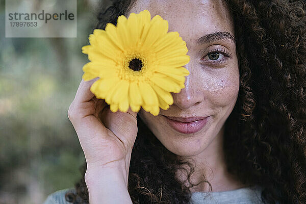 Lächelnde schöne Frau mit gelber Blume über dem Auge