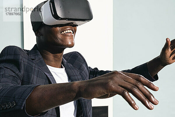 Glücklicher junger Mann mit Virtual-Reality-Brille vor der Wand