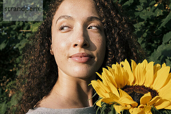 Lächelnde schöne Frau mit Sonnenblume  die das Sonnenlicht genießt