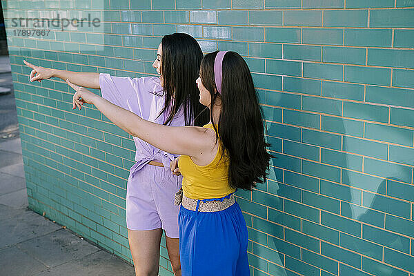 Young women pointing together near brick wall