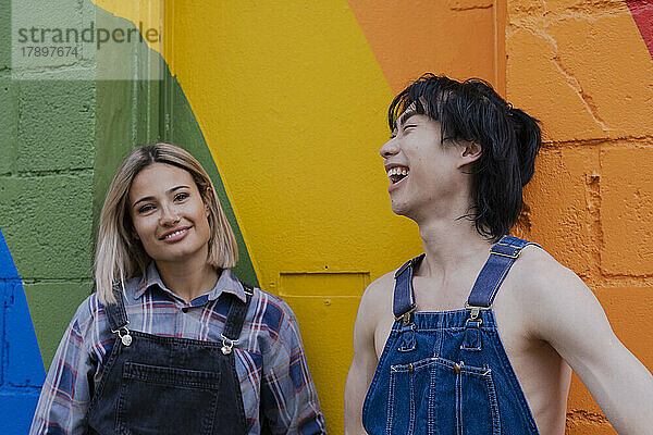 Junge Freunde hängen miteinander ab und stehen vor einem an die Wand gemalten Regenbogen