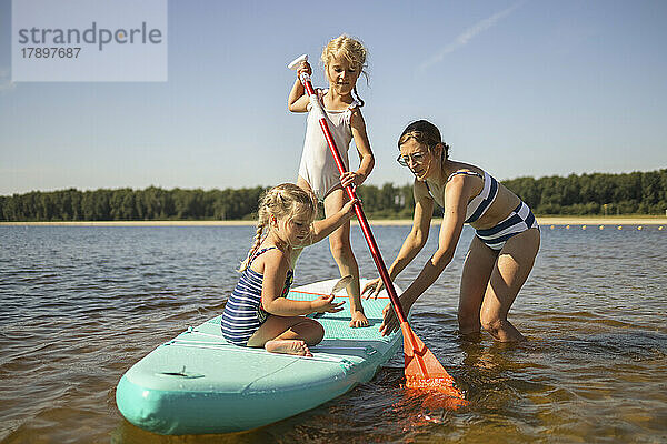 Mädchen mit Mutter auf Stand-Up-Paddle-Board inmitten des Sees