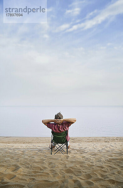 Mann sitzt entspannt auf Klappstuhl am Strand