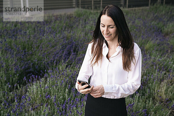 Glückliche reife Frau  die im Park ihr Mobiltelefon benutzt