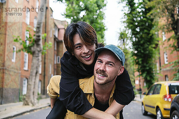 Lächelnder Mann huckepack mit seinem Freund in der Stadt