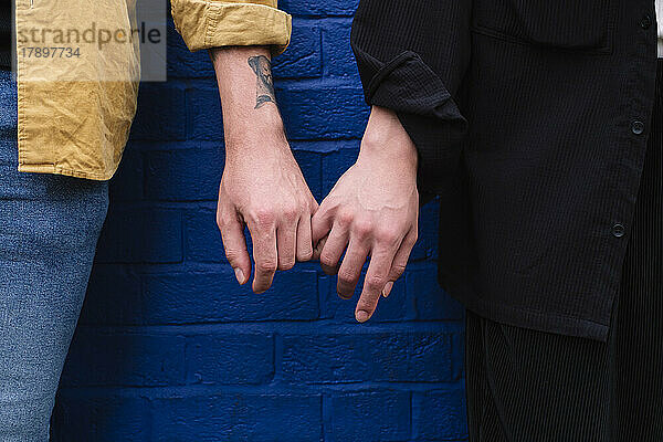 Schwules Paar hält Händchen und steht vor einer blauen Wand