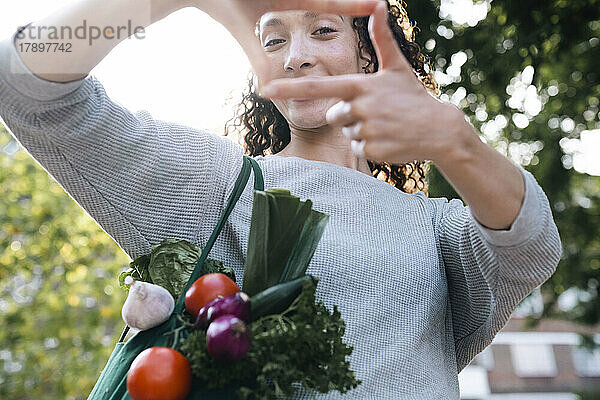 Frau mit einer Tüte Gemüse schaut durch den Fingerrahmen