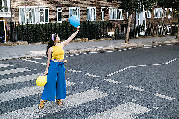 Frau mit erhobener Hand hält Luftballons und steht auf einem Zebrastreifen