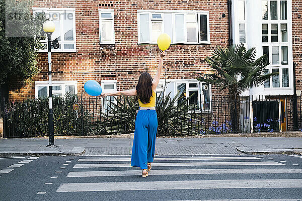 Frau mit Luftballons läuft auf Zebrastreifen in der Stadt