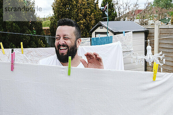 Fröhlicher Mann trocknet Laken auf der Wäscheleine im Hinterhof