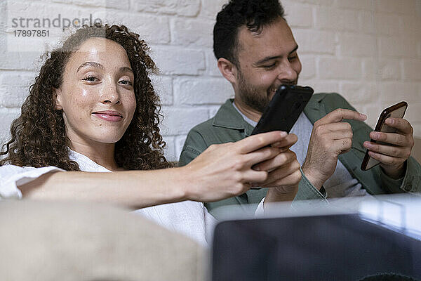 Lächelnde Geschäftsfrau mit Kollegin  die im Büro ihr Smartphone nutzt
