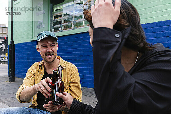 Lächelnder Mann stößt mit seinem Freund auf eine Bierflasche zu