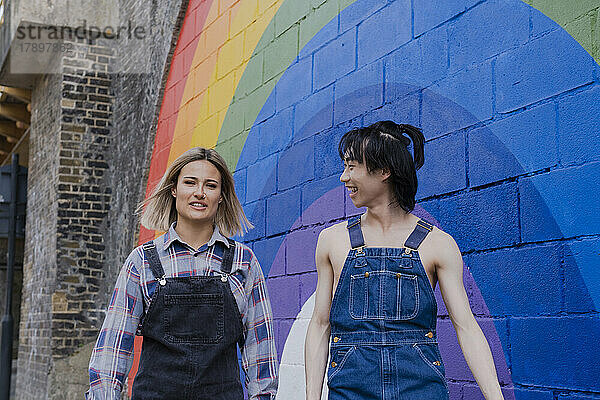 Junge Freunde gehen gemeinsam am Regenbogen entlang  der an die Wand gemalt ist