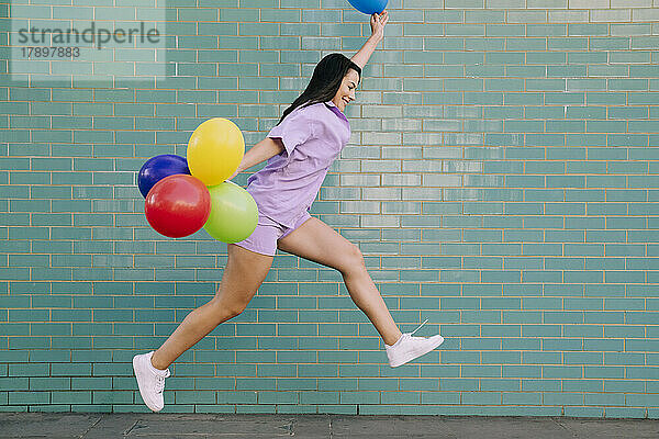 Sorglose junge Frau springt mit Luftballons an der Wand