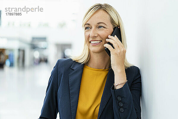 Lächelnde Geschäftsfrau  die am Telefon spricht und sich an die Wand lehnt