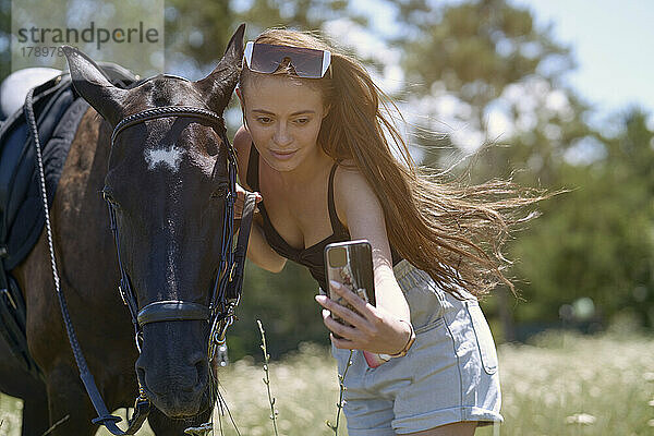 Schöne Frau mit Pferd macht an einem sonnigen Tag ein Selfie per Smartphone