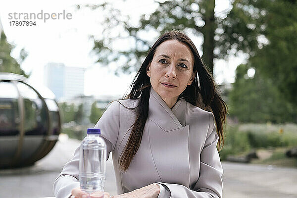 Geschäftsfrau mit Wasserflasche sitzt im Büropark