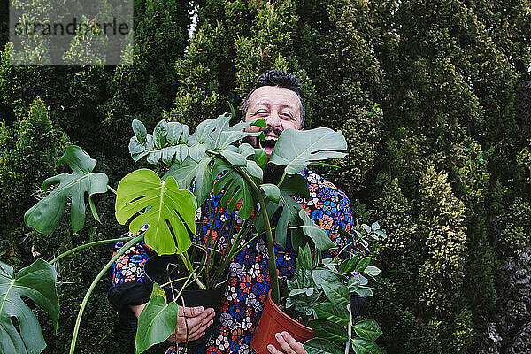Fröhlicher Mann trägt Topfpflanzen im Hinterhof