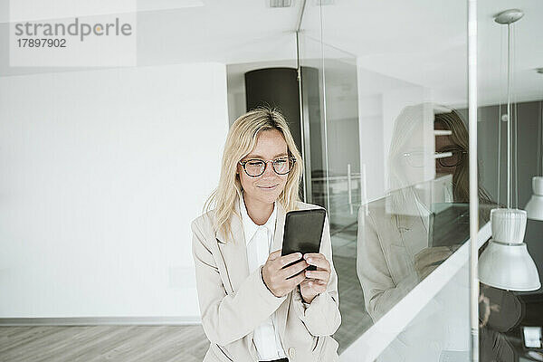 Geschäftsfrau mit Brille benutzt Mobiltelefon im Büro