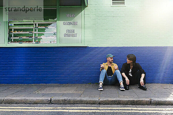 Mann unterhält sich mit Freund  der auf dem Bürgersteig sitzt