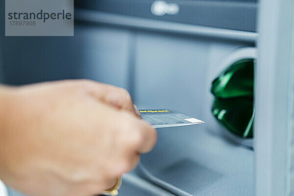 Hand of woman inserting credit card into ATM machine