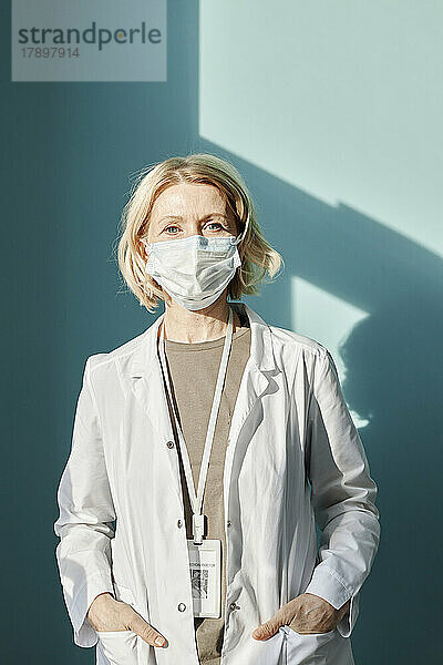 Reifer Arzt mit schützender Gesichtsmaske vor der Wand