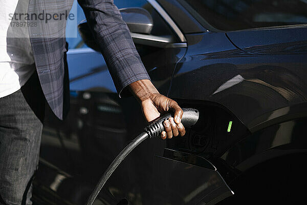 Hand eines Mannes  der das Ladegerät an ein Elektroauto anschließt
