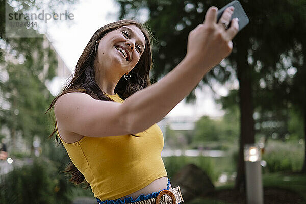 Lächelnde junge Frau  die im Park ein Selfie mit dem Smartphone macht