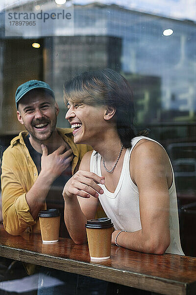 Fröhliche schwule Männer mit Kaffeetassen  gesehen durch das Fenster des Cafés
