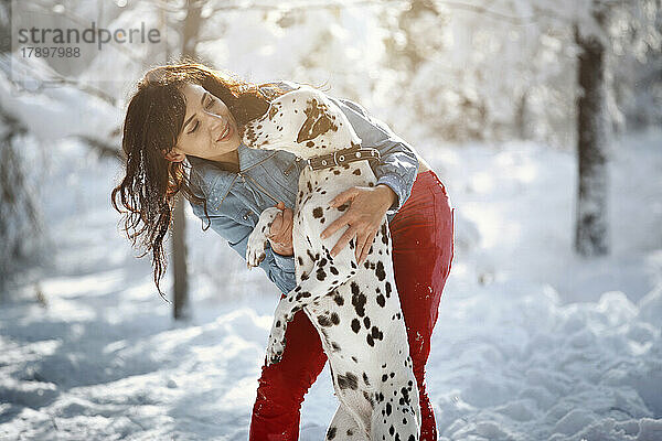 Lächelnde Frau umarmt dalmatinischen Hund im Winterpark