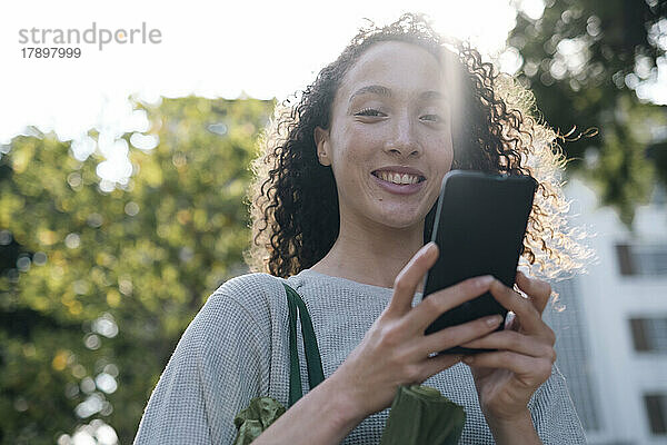 Lächelnde Frau  die an einem sonnigen Tag ihr Mobiltelefon benutzt