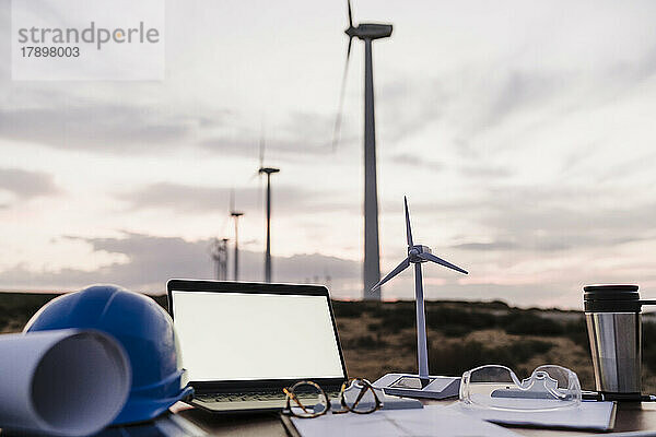 Windturbinenmodell per Laptop mit leerem Bildschirm auf dem Schreibtisch im Windpark