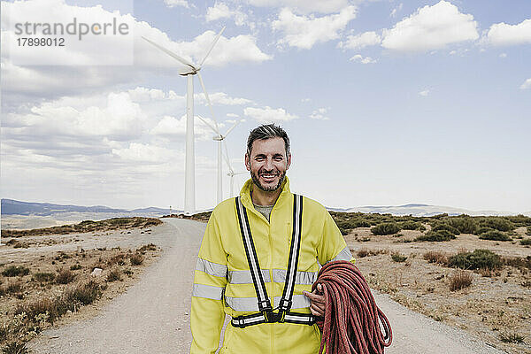 Lächelnder Techniker mit Seil steht am Windpark