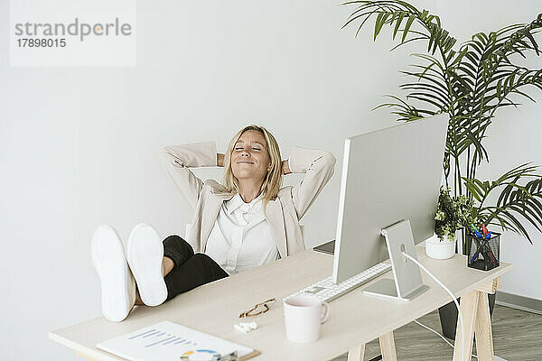 Entspannte Geschäftsfrau sitzt mit Füßen auf dem Schreibtisch im Büro