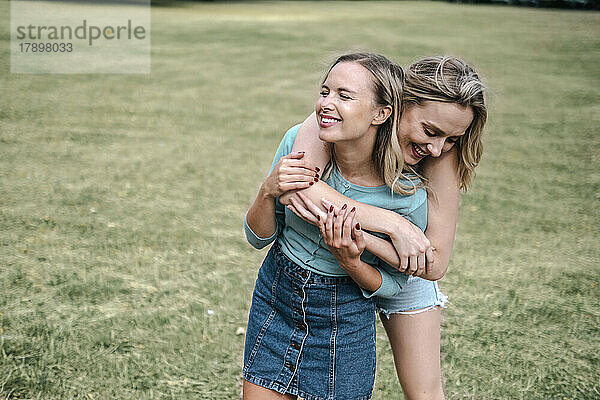 Glückliche blonde Frau umarmt Freundin im Park