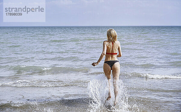 Frau läuft an einem sonnigen Tag im Meer am Strand