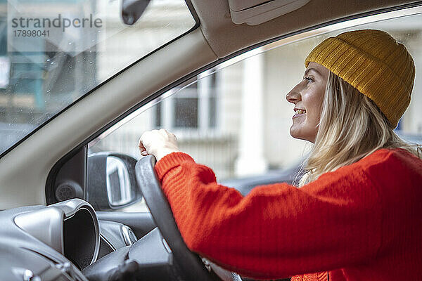 Lächelnde Frau mit Strickmütze fährt Auto